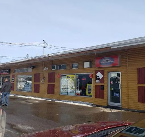 Façade d’un petit commerce avec vitrines et enseignes, devant un stationnement mouillé